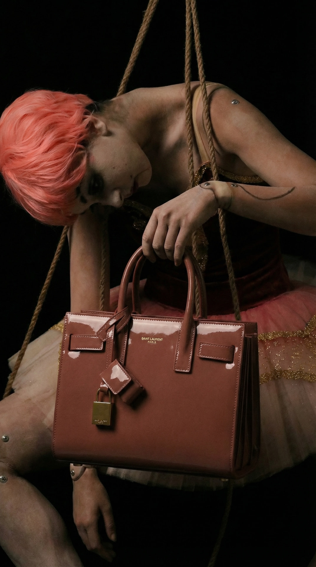 Model in a tulle skirt holding a rose patent leather top-handle bag in low light